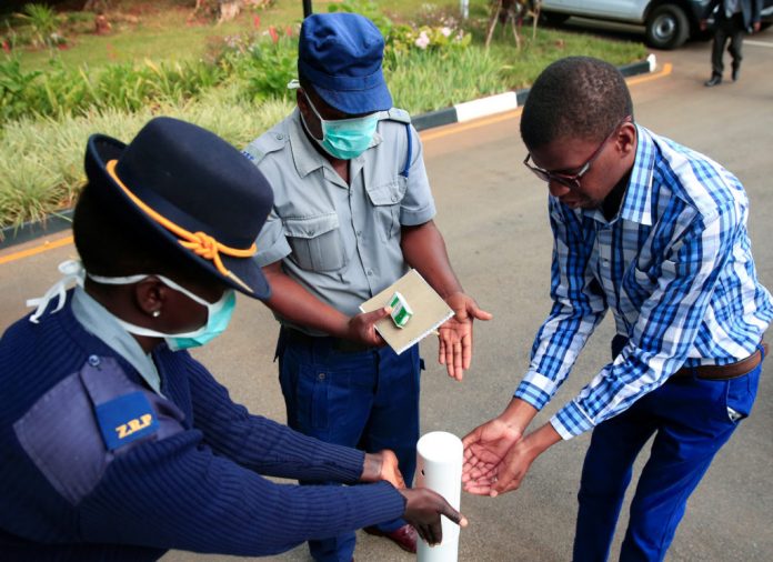 Police officer shows a visitor how to disinfect his hands against the spread of coronavirus disease (COVID-19) at State House in Harare
